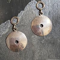 Pair of silver round disc earrings with center holes on a grey textured surface.