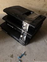 Stack of three black PlayStation 3 consoles taped together on floor