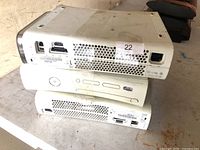 Stack of three white Microsoft Xbox 360 consoles showing ports and exterior wear