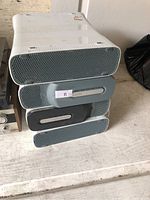Stack of four white Microsoft Xbox 360 consoles, one with attached grey HDD, no accessories visible