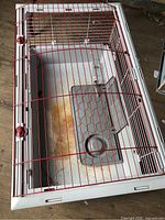 Top view of rectangular plastic-base cage with red wire lid and interior platform