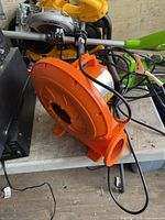 Overall view of orange electric blower showing housing, intake grille, outlet, cord and handle