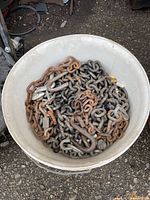 Top view of white bucket filled with assorted steel chains showing mixed rusted and galvanized links
