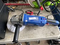 Overall view of blue corded electric buffer polisher with side handle and buffing pad on workbench
