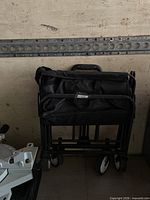 Folded black collapsible wagon showing metal frame, fabric body, four wheels and handle