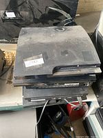 Stack of four dusty PlayStation 3 Slim consoles, partial power cord shown
