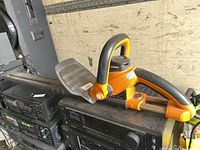 Side view of orange and black corded hedge trimmer resting on stereo equipment