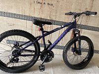 Left side view of purple Huffy youth mountain bike showing drivetrain, wheels, frame, saddle, pedals