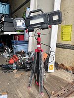 Front view of Husky LED work lamp mounted on red tripod with power cord visible.