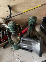 Lot view showing two green kerosene lanterns and grey handheld spotlight