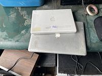 Stacked view of two worn Apple laptops showing top covers and exterior condition