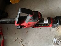 Left side view of Milwaukee M12 Fuel cordless chainsaw showing handle, bar, and battery