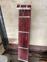 Full view of red aluminum toboggan leaning against wall