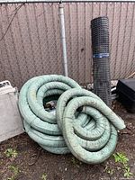Coiled green perforated drain pipe and standing roll of black dimpled membrane