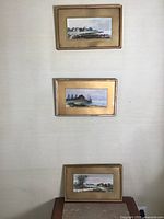 Photo showing all three framed watercolors hung vertically on a wall, each framed in gold-tone frames with mats.