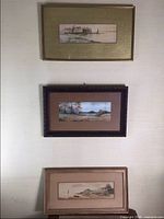 Full view of three framed watercolor paintings hanging on wall, depicting coastal houses and ocean scenes.