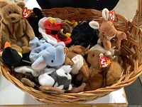 Wicker basket filled with various Beanie Babies including bear, elephant, panther, bird, deer, and others with original TY tags.