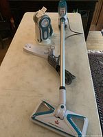 Full view of the Bissell PowerFresh Slim stick vacuum with charging base and Black & Decker handheld vacuum on a table.