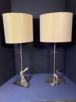 Pair of table lamps with brushed nickel bases and oval pleated paper shades shown together on a dark background.