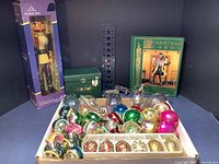 Wide shot of over 30 Christmas items including several vintage mercury glass ornaments, boxed nutcracker, Snowbabies Frosty figurine, silver plate lions, and Dickens book.