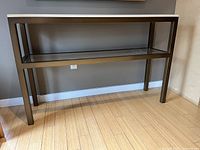 Front and side view of the console table displayed against a grey wall, showing the stone top and metal base with lower shelf