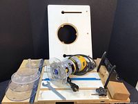 DeWalt router with clear plastic guide plates, adjustable router table, wrench, and sliding fence in view.