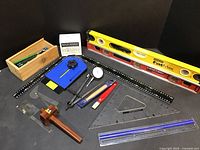Full view of all tools including Stanley levels, Rockler gauge, rulers, squares, dial indicator, and wooden storage box with marking pencils.