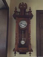 Full frontal image of vintage wooden wall clock including pendulum and carved eagle top.