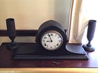 Full view of Gilbert mantle clock with arched top and attached base along with two turned wood candleholders placed on each side and winding key in front.
