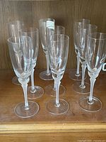 Front view of nine champagne flutes arranged on a wooden shelf, showing the tall, slender shape and intricately designed stems characteristic of the Gorham Newport pattern.