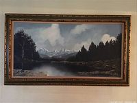 Full view of large framed canvas painting showing a landscape with trees, lake, and mountains under cloudy sky