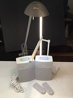 Photo showing two Bose SoundTouch 10 wireless speakers, white, with mesh front and control panel on top, plus two remote controls, a white desk lamp and black telescoping desk lamp behind them.
