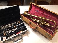 Both instruments together showing the trumpet in open brown hard case with red velvet lining and the clarinet in a black hard case with accessories.