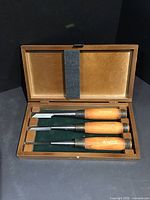 Top-down view of three wood chisels in wooden box, showing blades and handles.