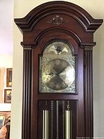 Full view of the upper part of the grandfather clock showing the wooden arch and brass clock face