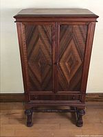 Front view of antique wooden radio cabinet with geometric veneer door panels and carved legs.