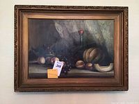 Framed still life oil painting on canvas depicting various fruits with a dark draped background, showing the entire piece including the thick ornate frame.