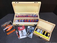 Wide view showing the large Yonico router bit set in wooden case, smaller wooden box with 5 yellow-coated bits, and packaged router bits from CMT, Whiteside, and Rockler.