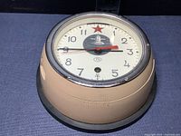 Full view of the submarine commander's clock showing beige metal case and black mounting base with clock face visible.