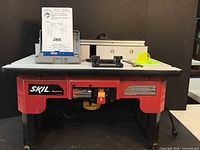Front view of router table with Skil RAS900 label and instruction manual on table top.