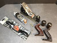 Wide view showing Stanley Bailey No.4 plane, Ace Hardware plane in packaging, Stanley spokeshave, spare wooden knobs, screws, and parts.