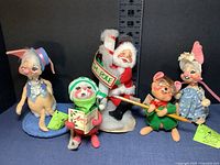 Front view of all five dolls showing their size ranging from 5.5 to 8.5 inches with holiday theme props and attire.