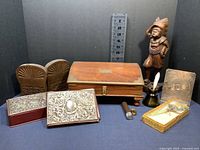 Full view of the lot showing wooden box, wooden figurine, two silverplate items, jade handled magnifying glass in box, bookends, ink pot with quill, and cigar holder