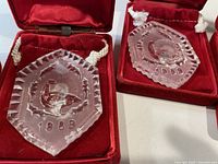 Close-up of two hexagonal crystal ornaments from 1989 with detailed etchings and year markings, stored in red velvet cases.