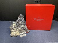 Crystal figurine of Santa Claus sitting on a park bench next to a sack, with original Waterford Crystal red box showing wear.