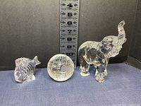Three clear crystal Waterford figurines - tropical fish, spherical world paperweight, and an elephant figurine on blue cloth background indicating size with ruler