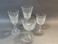 Four Waterford Lismore crystal glasses displayed: a sherry glass, a white wine glass, a cocktail glass, and a port wine glass, showing the variety in shape and size with detailed diamond cuts.