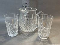 Two water glasses flanking the Lismore Ice Lip pitcher against a neutral background with ruler visible.