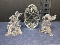 Photo showing two Waterford crystal bunny figurines and one crystal egg paperweight on blue fabric with vertical ruler indicating heights