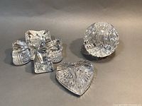 Three Waterford crystal pieces: shamrock paperweight, heart paperweight, and spherical ball candle holder displayed on neutral surface.